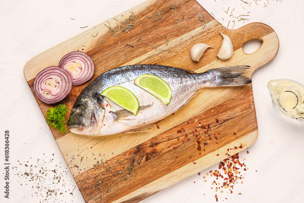 Wooden board of raw dorado fish with lemon and onion on light background