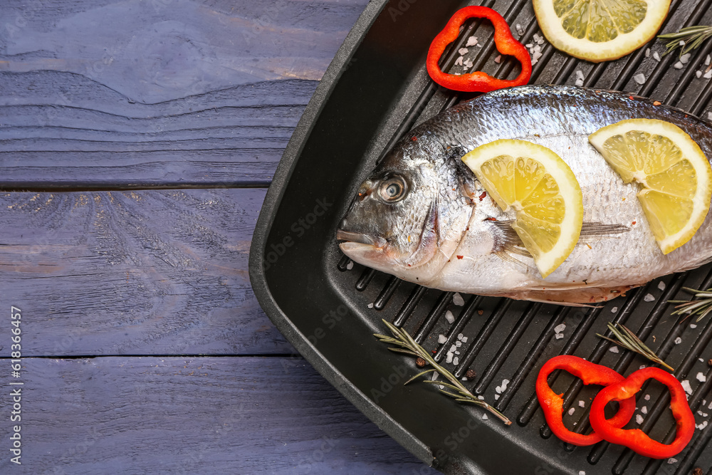 Grill pan of raw dorado fish with lemon on grey wooden background