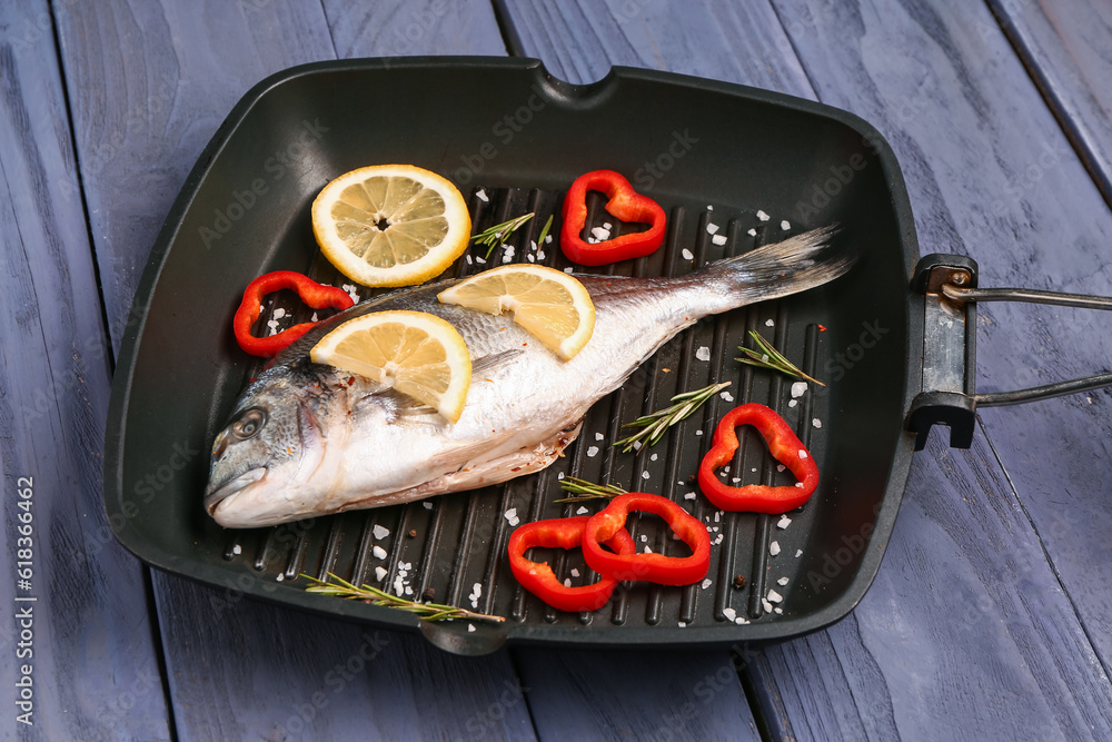 Grill pan of raw dorado fish with lemon on grey wooden background