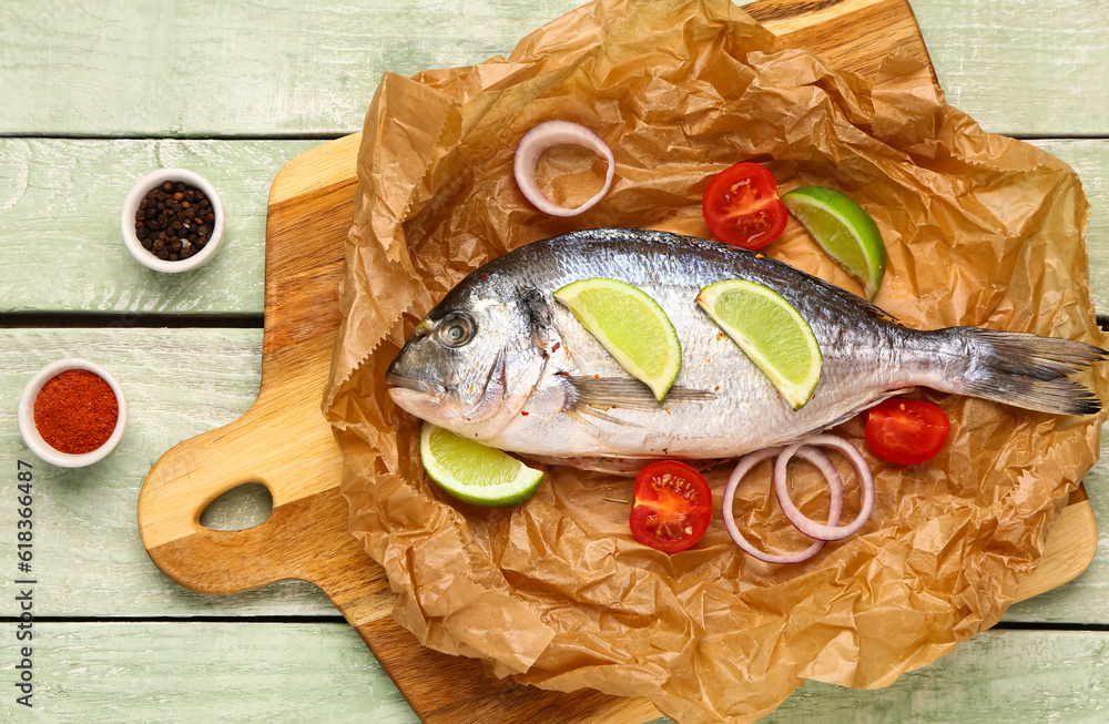 Board of raw dorado fish with lime, onion and spices on green wooden background