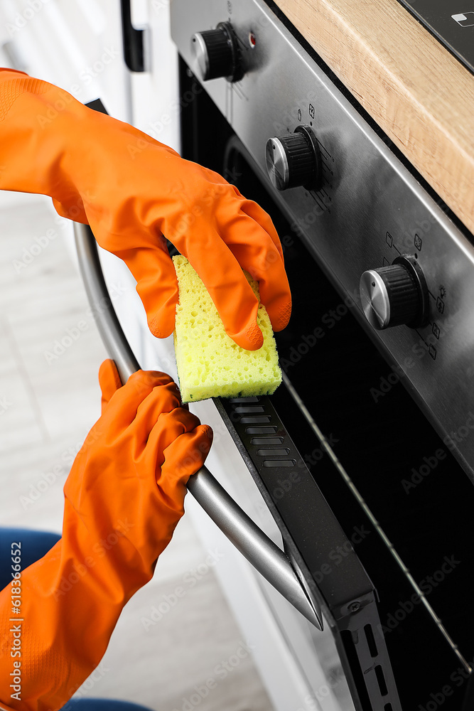 Woman in orange rubber gloves cleaning electric oven with sponge