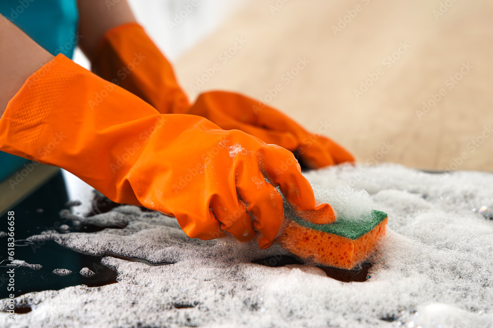 Woman in orange rubber gloves cleaning electric stove with sponge