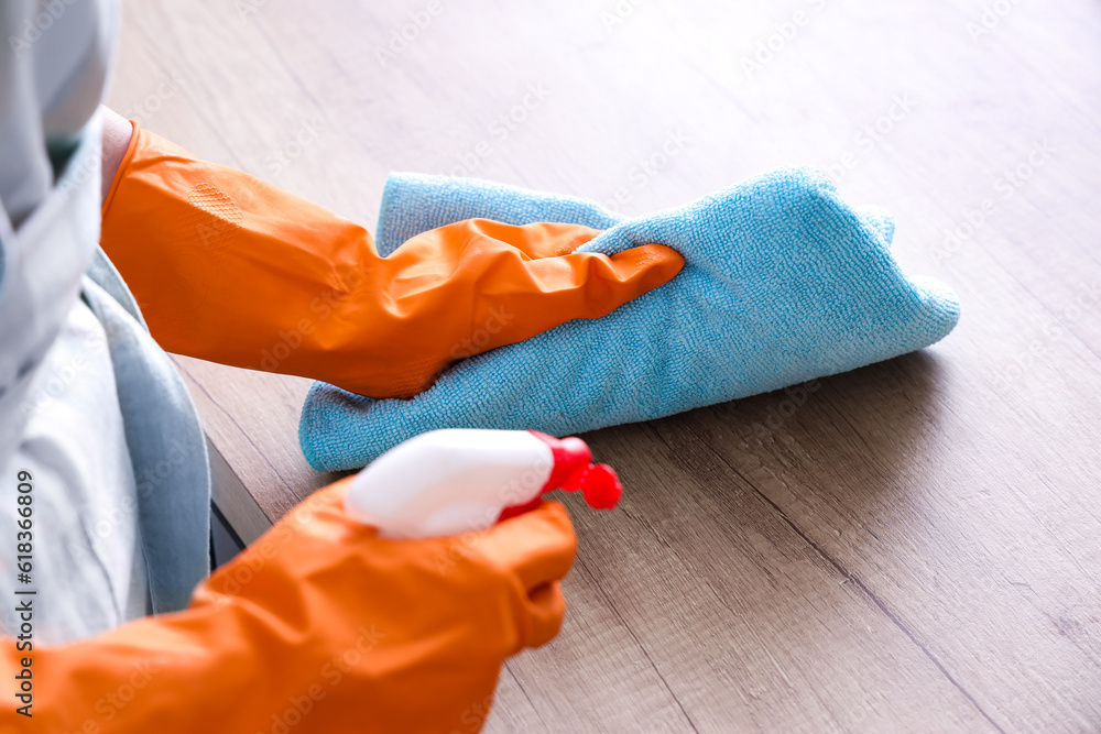 Woman in orange rubber gloves cleaning wooden countertop with rag and detergent