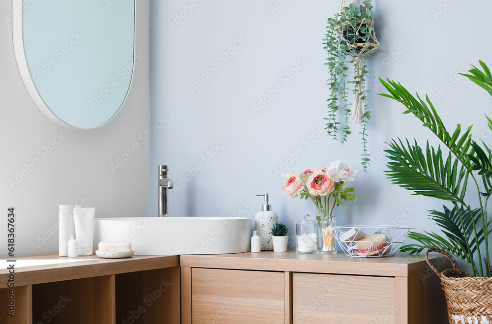 Interior of light bathroom with sink bowl, bath accessories, houseplants and ranunculus flowers