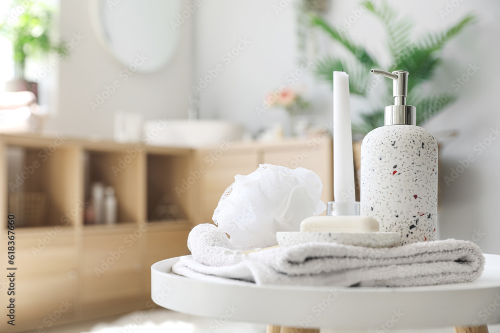 Soap bar, dispenser, shower sponge, towel and candle on table in bathroom, closeup