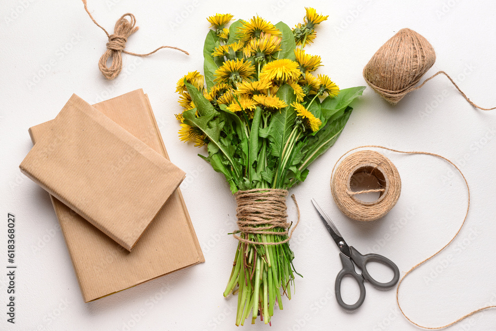 Bouquet of beautiful dandelion flowers, rope, scissors and books on light background