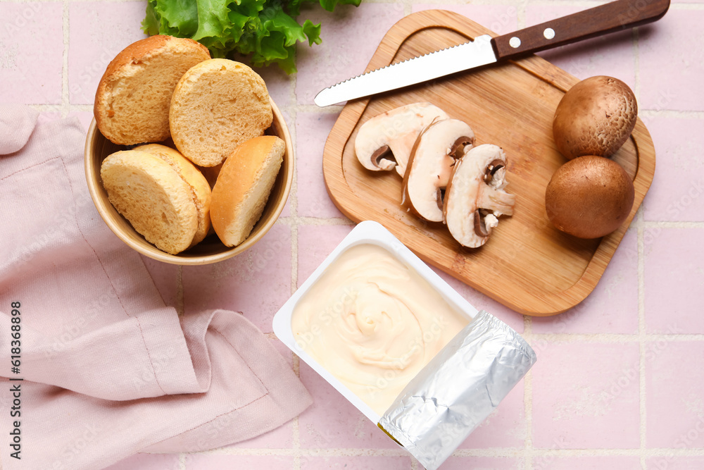 Plastic container with tasty cream cheese, mushrooms and croutons on pink tile background