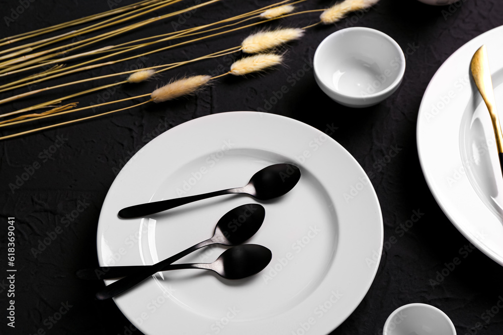 Clean plate, spoons and dried lagurus on black table