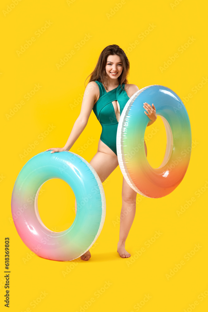 Young woman with swim rings on yellow background