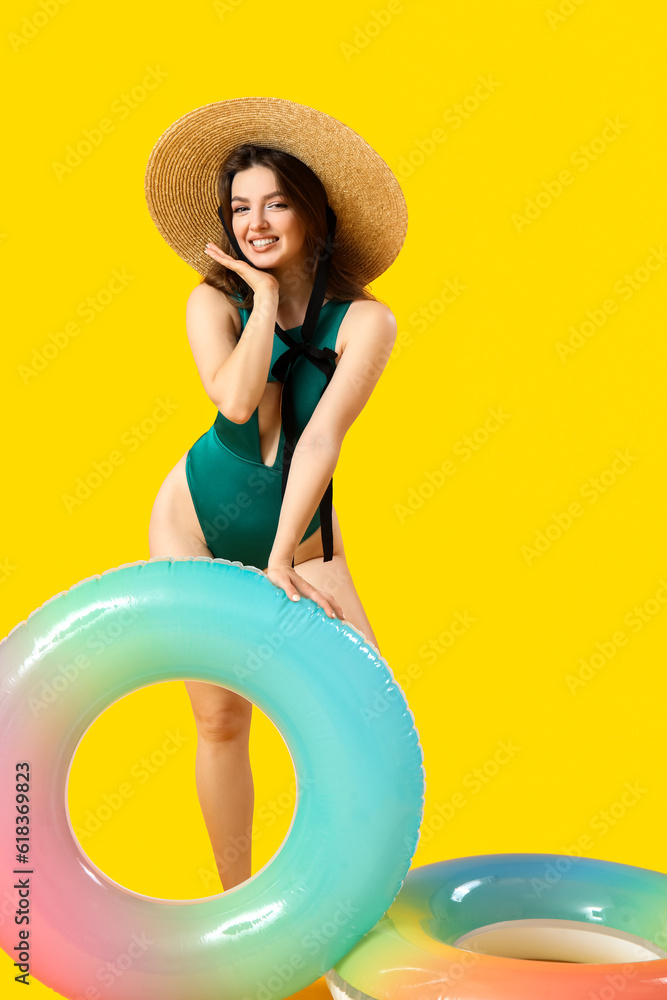 Young woman with swim rings on yellow background