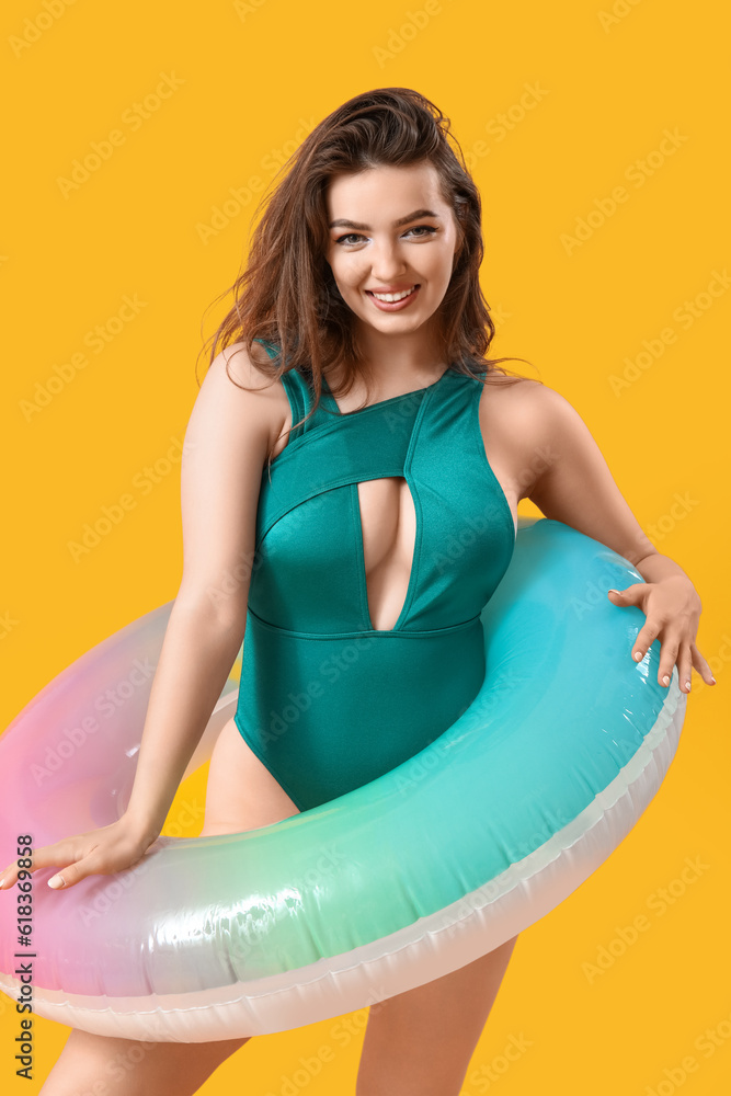 Young woman with swim ring on yellow background