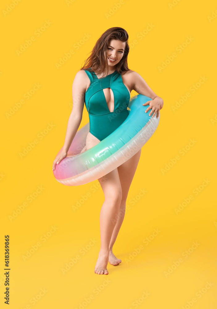 Young woman with swim ring on yellow background