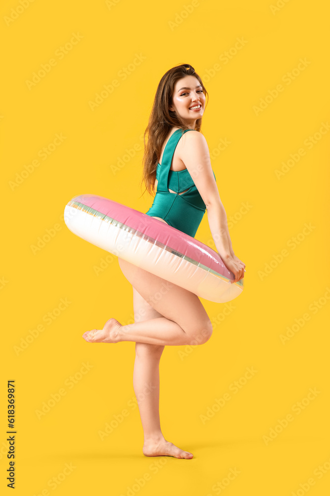 Young woman with swim ring on yellow background