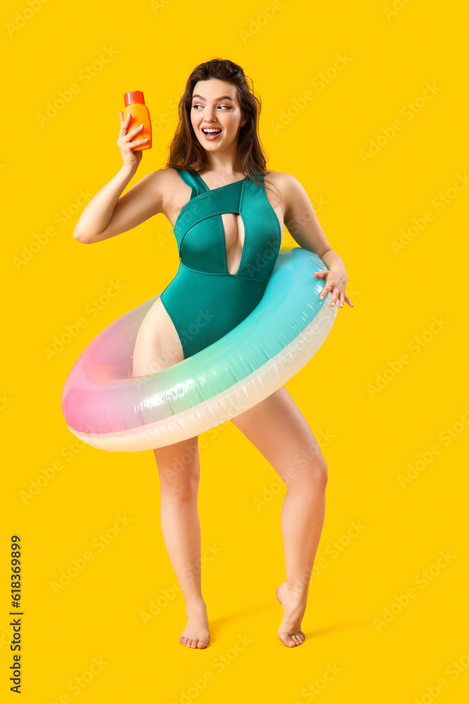 Young woman with sunscreen cream and swim ring on yellow background