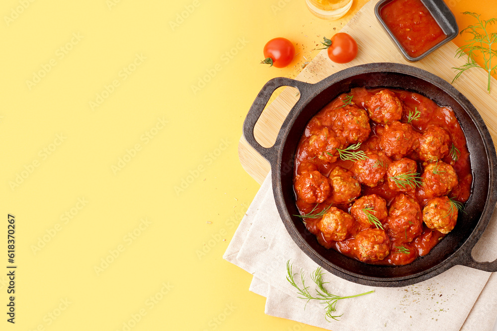 Frying pan of tasty meat balls with tomato sauce and dill on yellow background