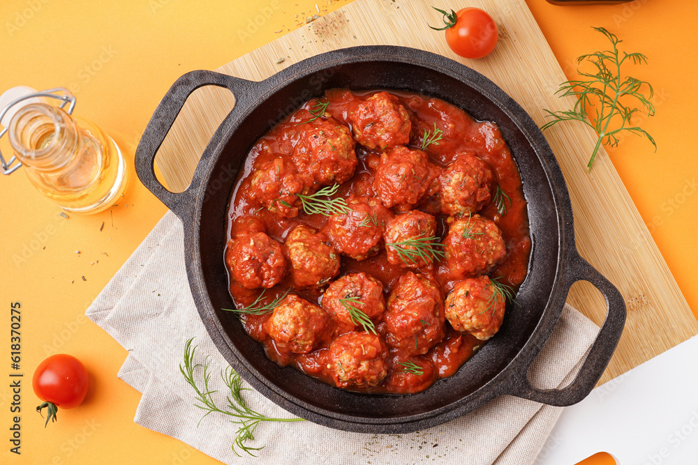 Frying pan of tasty meat balls with tomato sauce and dill on yellow background