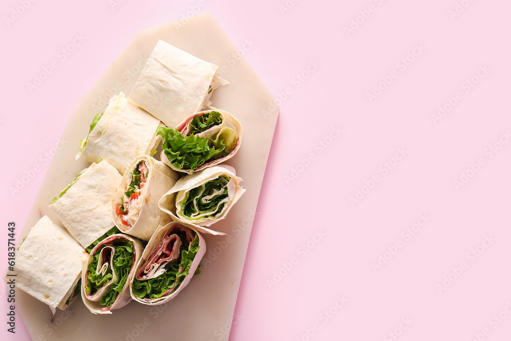 Board of tasty lavash rolls with sausages and greens on pink background