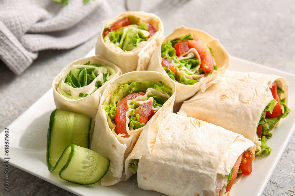 Plate of tasty lavash rolls with vegetables on grey background