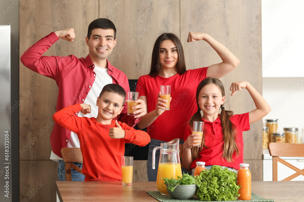 Happy family with orange juice showing muscles in kitchen