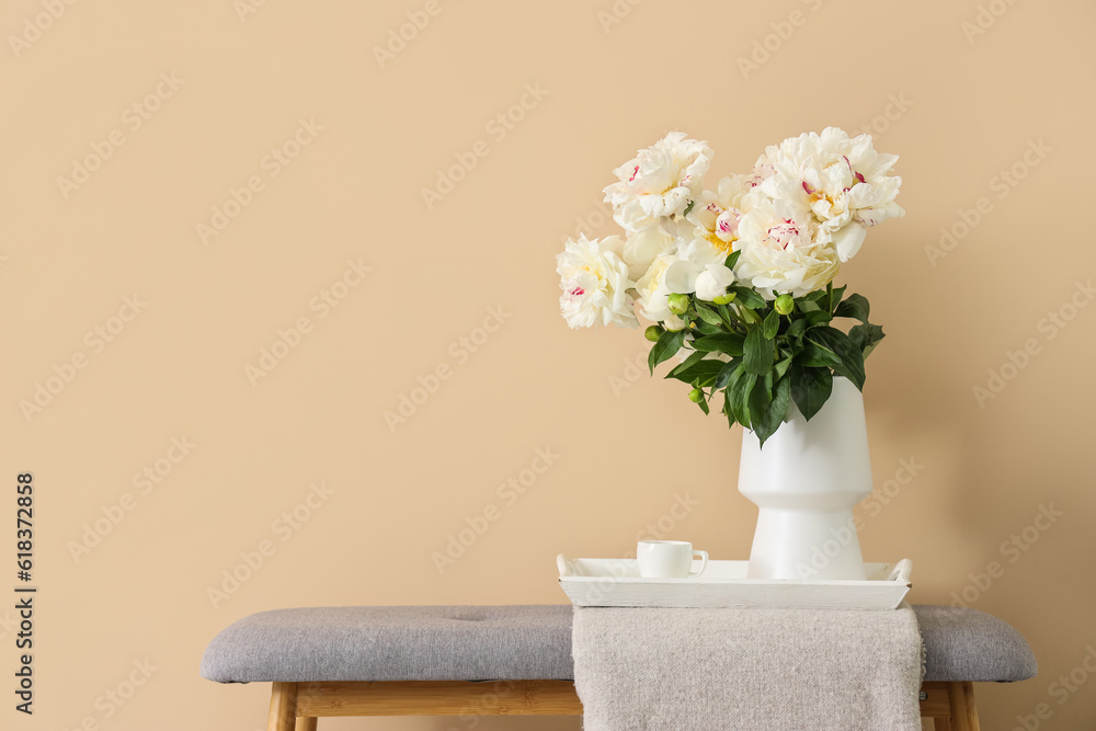 Vase of white peonies with cup of coffee on tray near beige wall