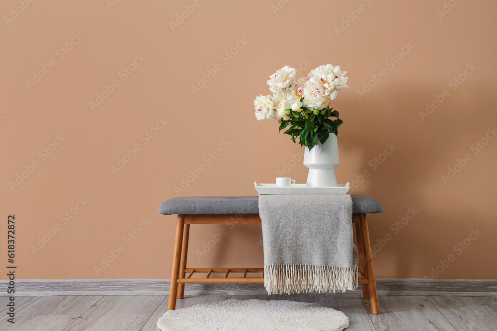 Vase of white peonies with cup of coffee on tray near beige wall