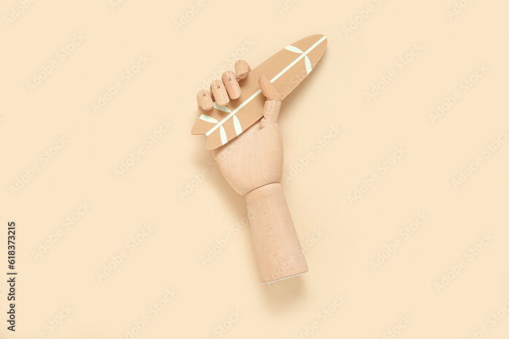 Wooden hand with mini surfboard on beige background