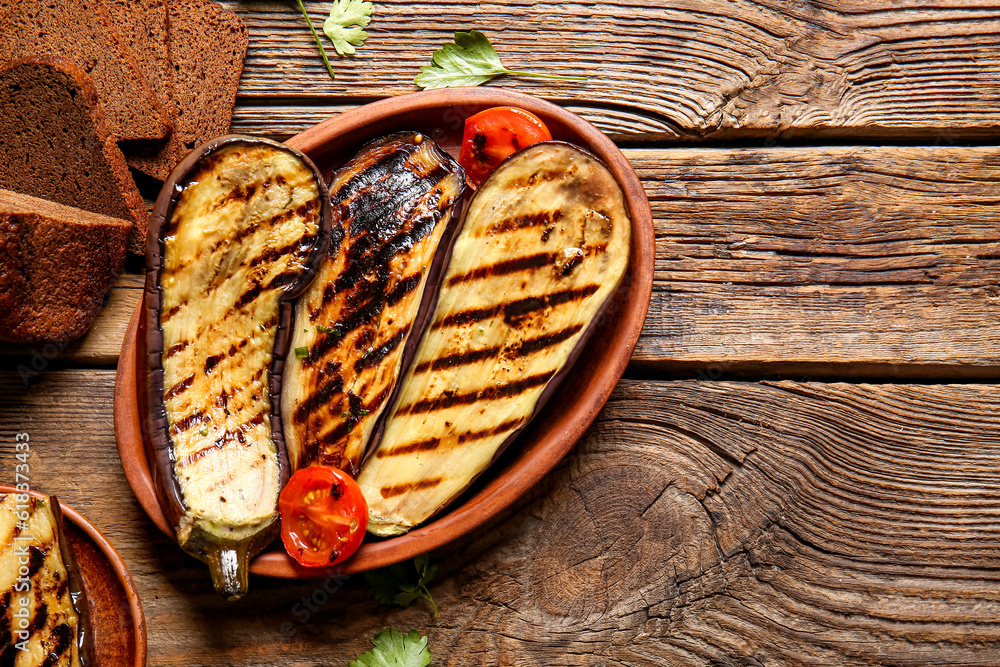 Plate with delicious grilled eggplants, tomatoes and bread on wooden background