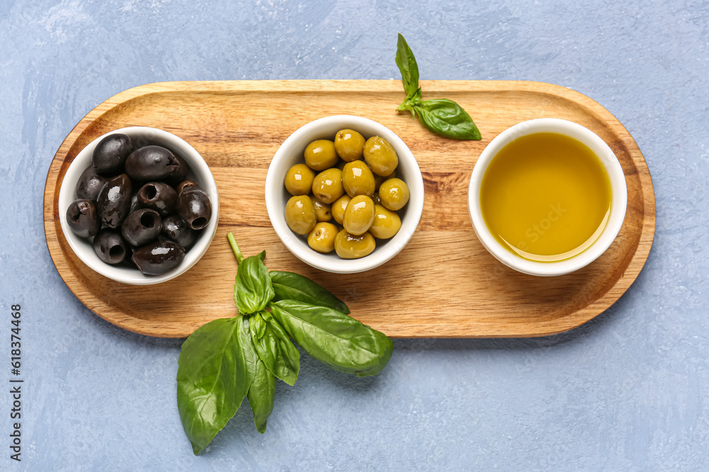 Bowls with ripe olives and oil on blue background