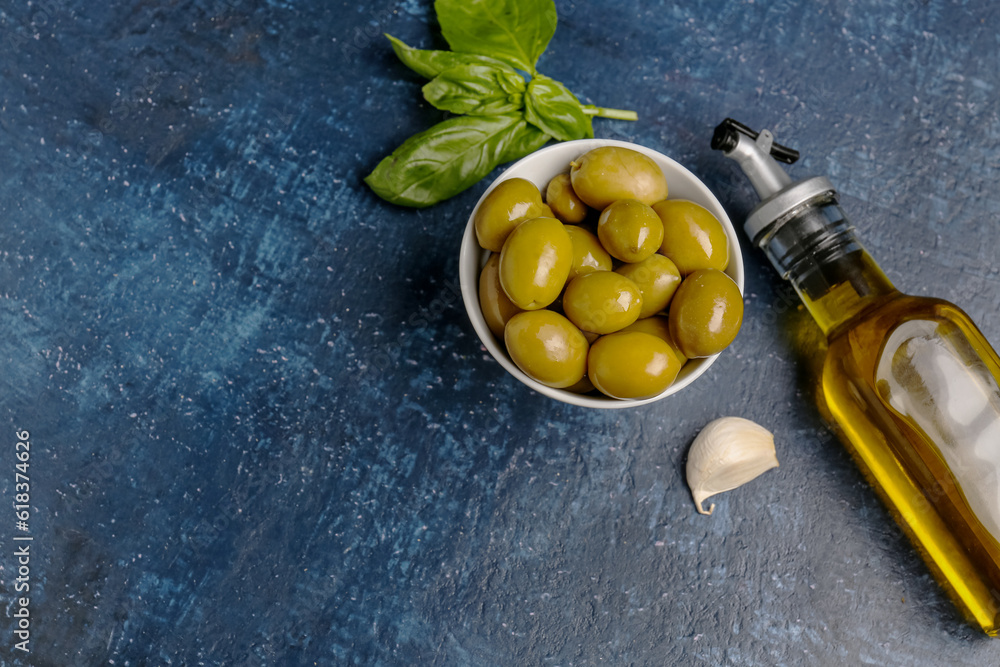 Bowl with ripe olives and bottle of oil on blue background