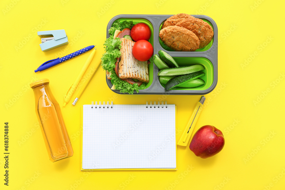 Stationery, blank notebook, drink and lunch box with tasty food on yellow background