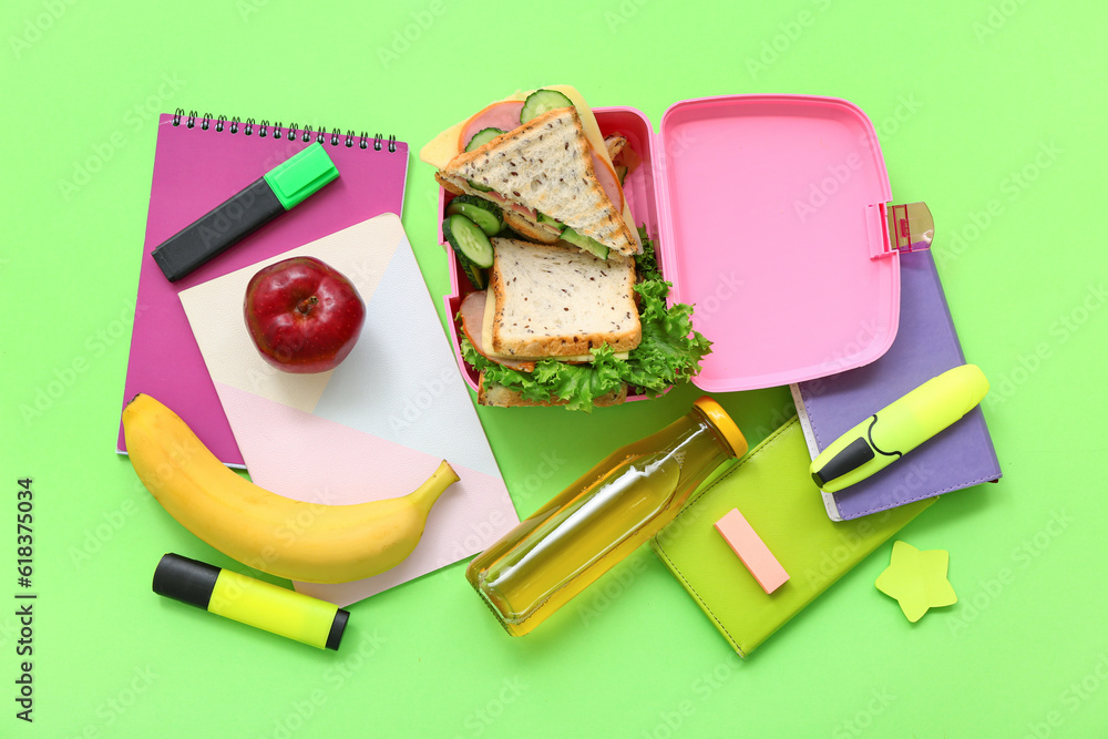 Different stationery, drink and lunch box with tasty food on green background