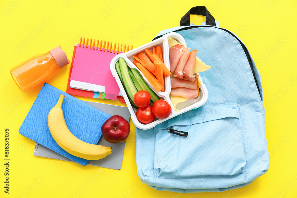 Backpack, stationery, drink and lunch box with tasty food on yellow background