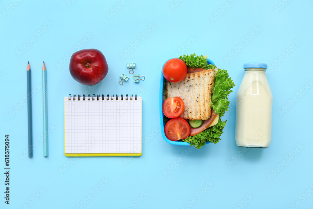 Stationery, drink and lunch box with tasty food on blue background