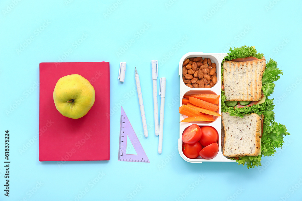 Stationery and lunch box with tasty food on blue background