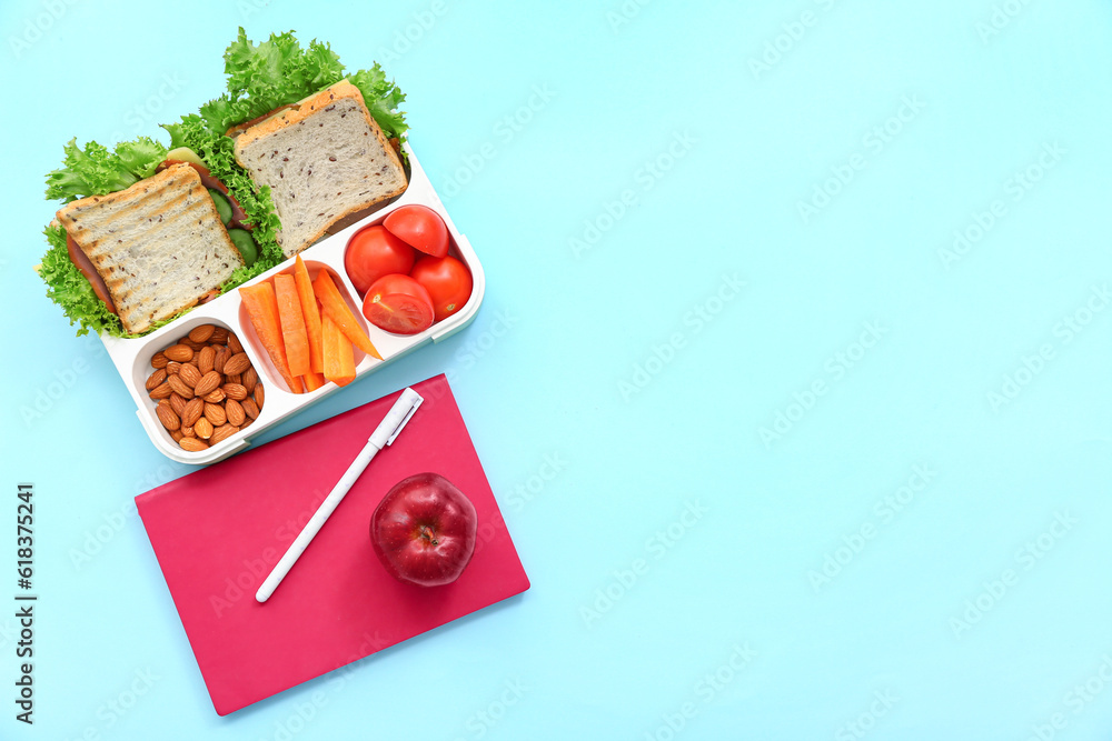 Stationery and lunch box with tasty food on blue background