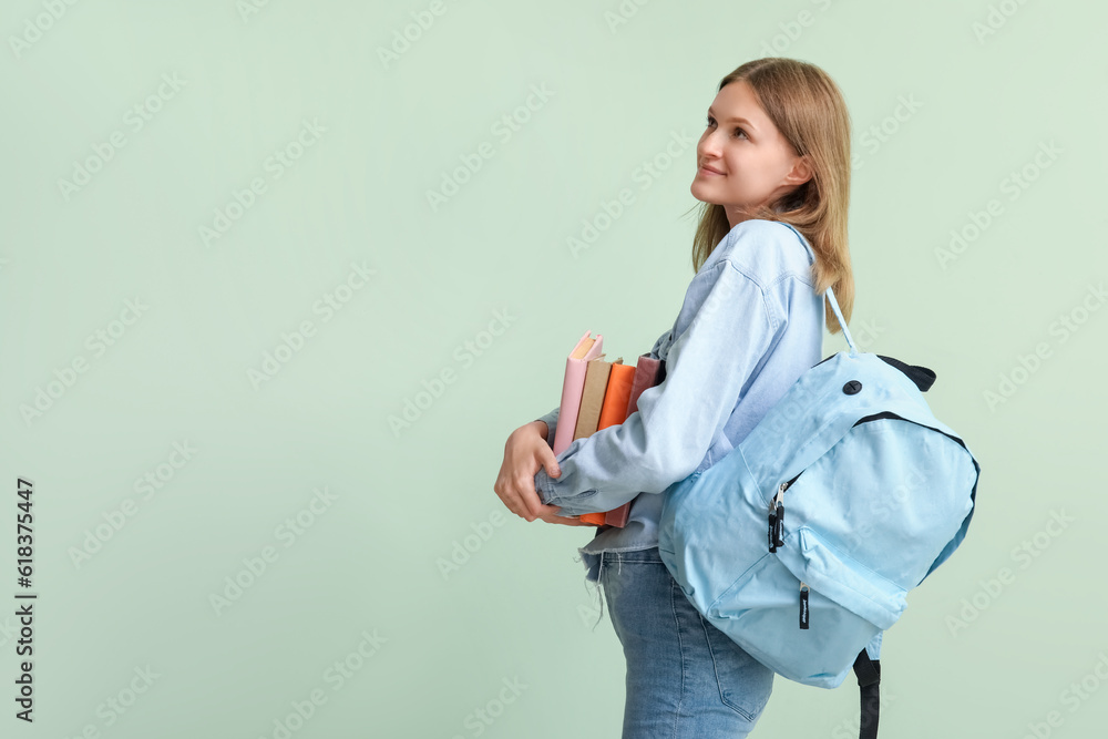 Female student with books and backpack on green background