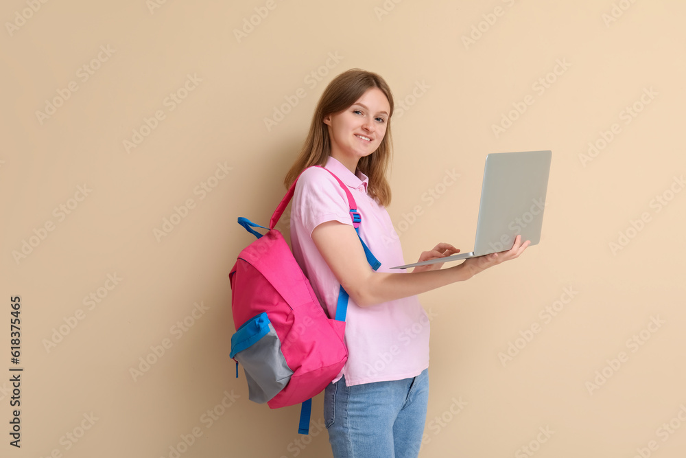 Female student with backpack using laptop on beige background