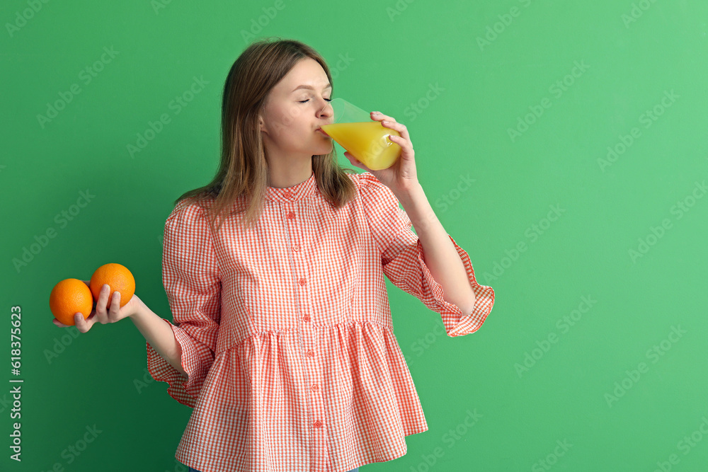 Teenage girl with oranges and glass of juice on green background