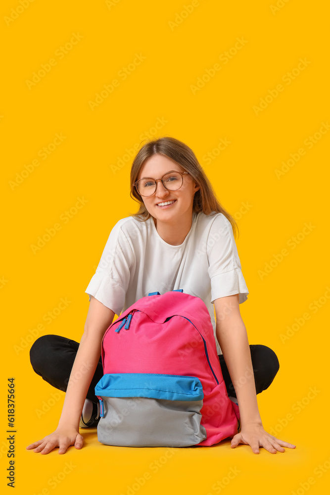 Female student with backpack sitting on yellow background