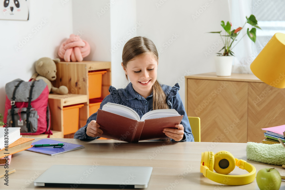 Little girl reading schoolbook at home