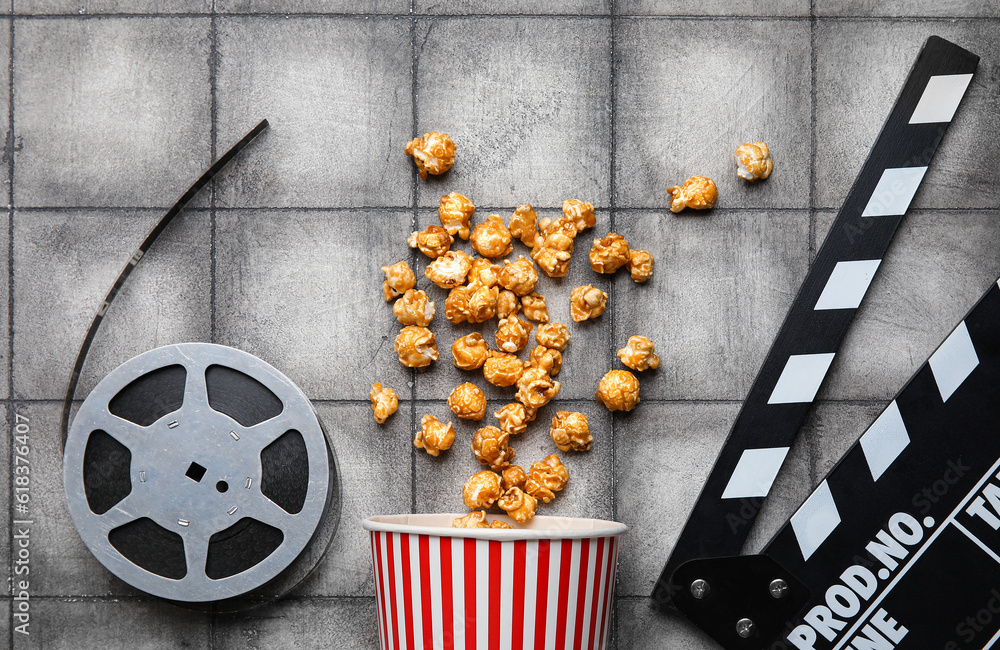 Bucket with tasty popcorn, clapperboard and film reel on grey tile background