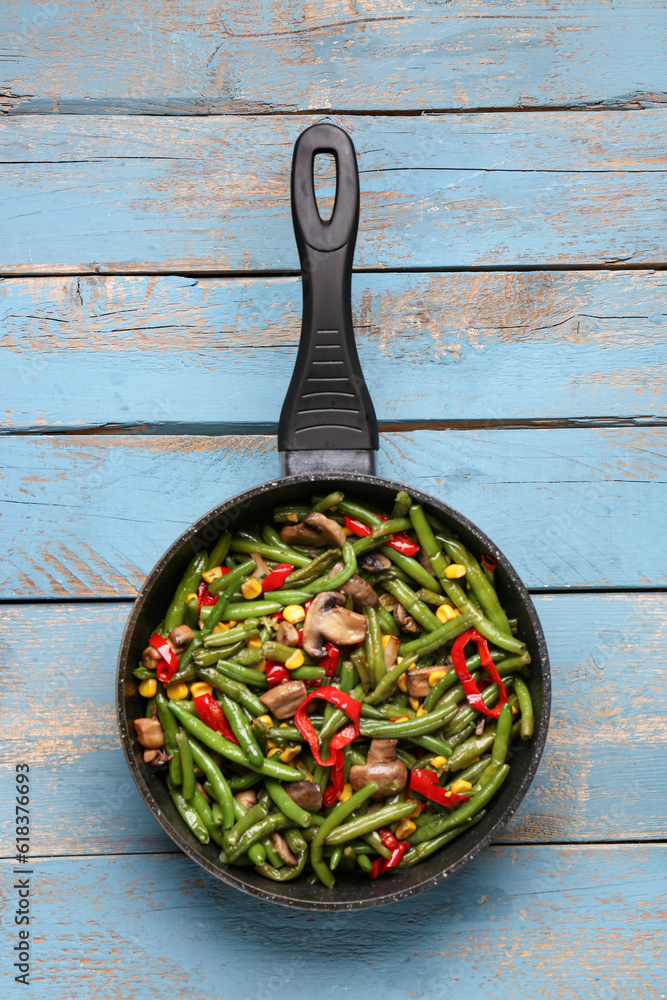 Frying pan with different vegetables on blue wooden background