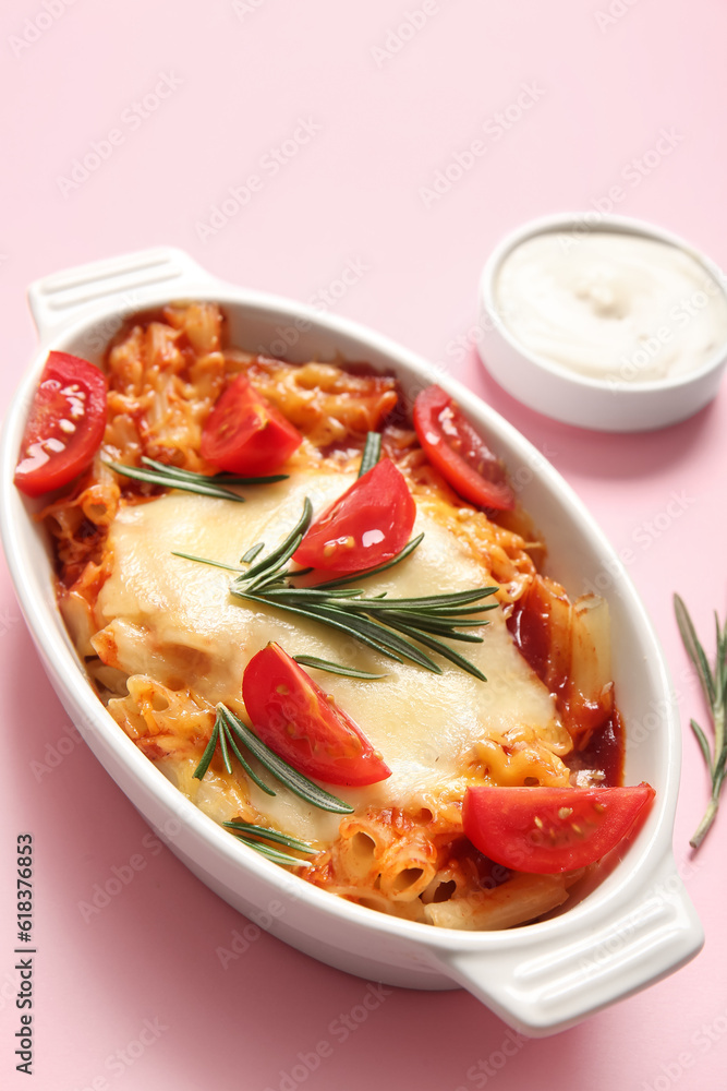 Baking dish of pasta with tomato sauce and cheese on pink background