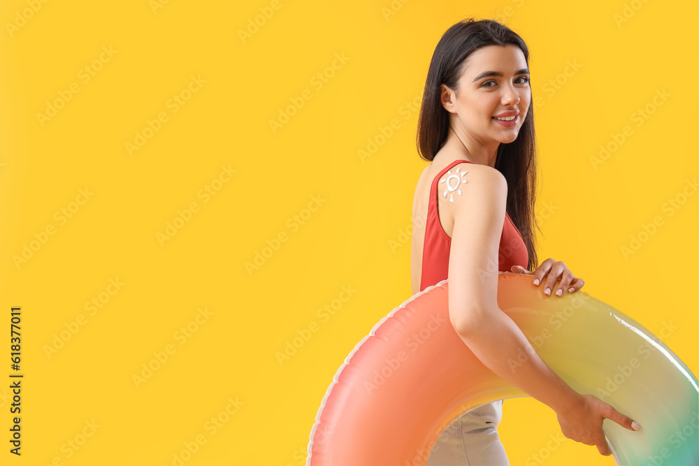 Young woman with sun made of sunscreen cream on her shoulder against yellow background