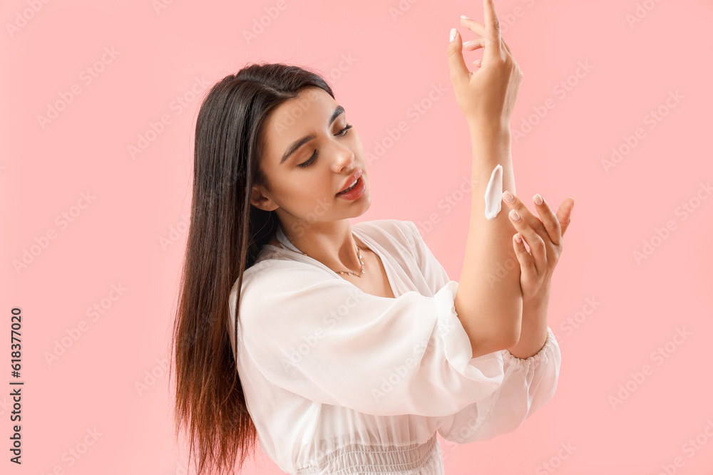 Young woman applying sunscreen cream on pink background