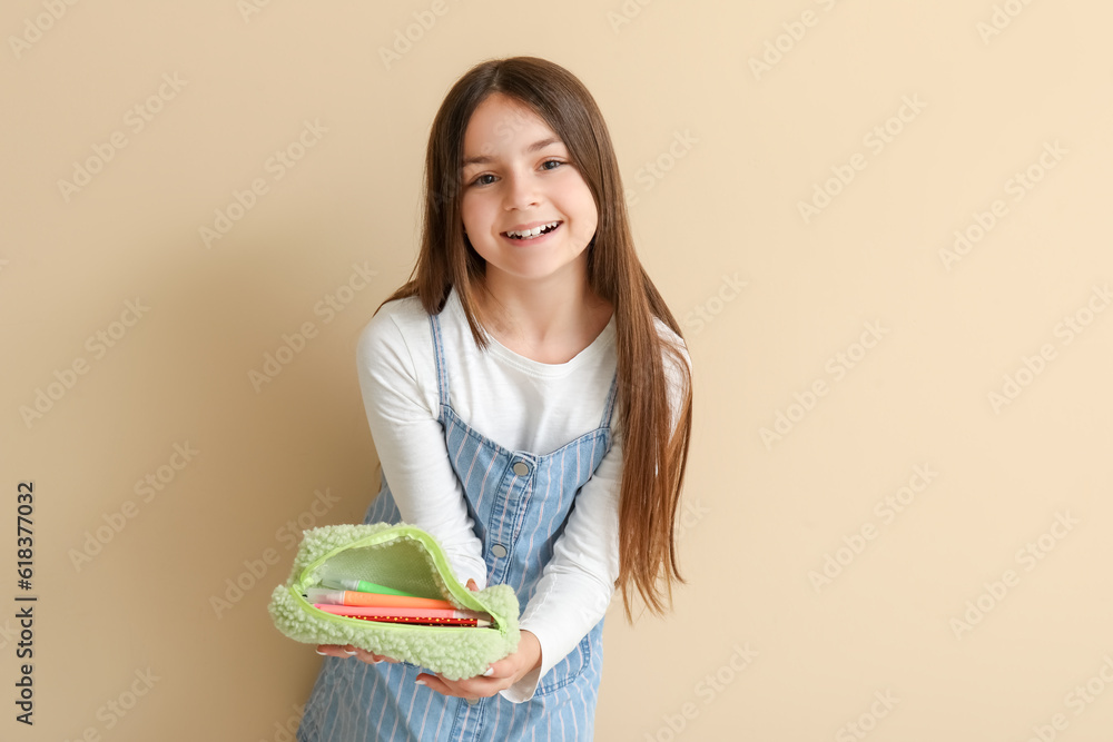 Little girl with pencil case on beige background