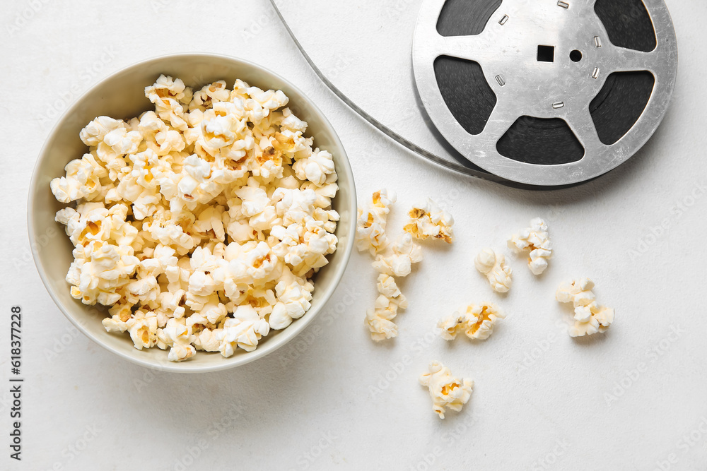 Bowl with tasty popcorn and film reel on white background