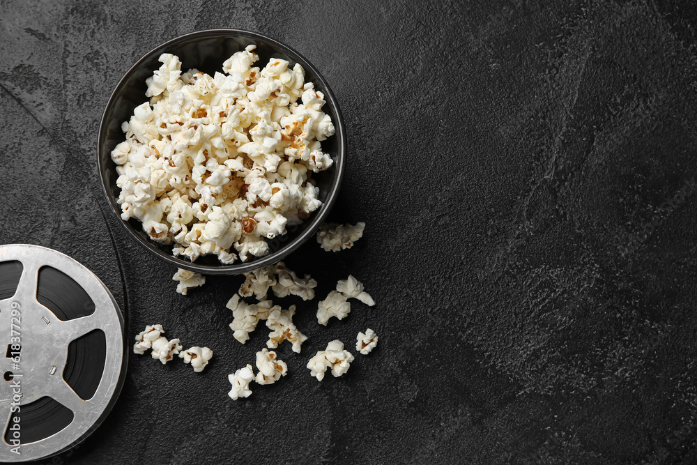 Bowl with tasty popcorn and film reel on black background