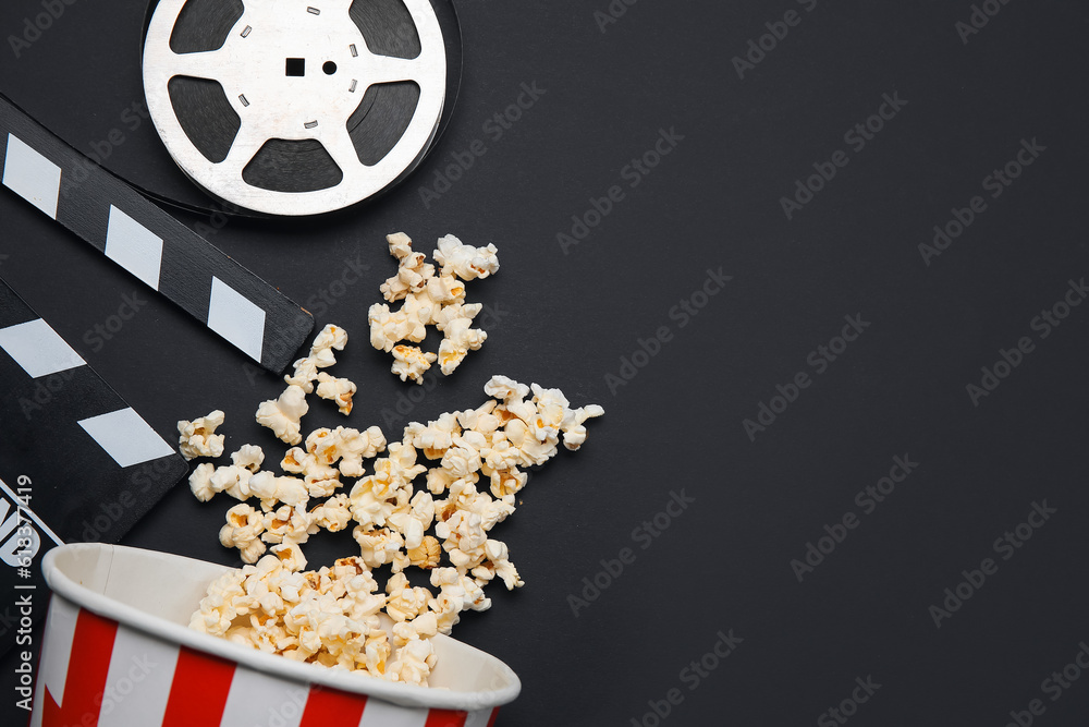 Bucket with tasty popcorn, clapperboard and film reel on black background