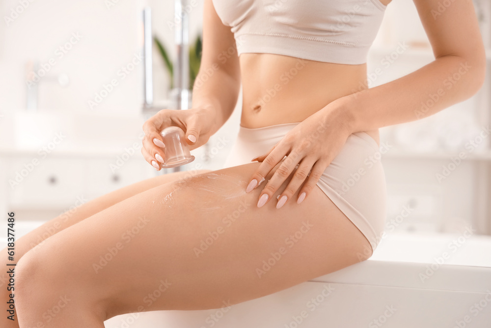 Young woman massaging her leg with anti-cellulite cup in bathroom, closeup